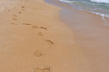 Clear emerald green sea with white foam and yellow sand on the beach with human footprints