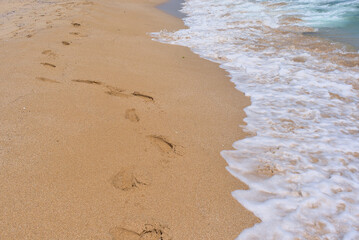 Clear emerald green sea with white foam and yellow sand on the beach with human footprints
