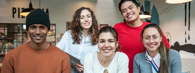 Fototapeten Horizontal banner or header with smiling multiethnic coworkers looking at camera making team picture in multifunctional room of the pizza restaurant for working brunch - Diverse work group © Davide Zanin