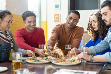 Obraz na płótnie Canvas Smiling friends eating pizza at modern pizzeria restaurant - Friendship concept with multi ethnic people enjoying time together having fun at pizzeria with pizza and beer pints