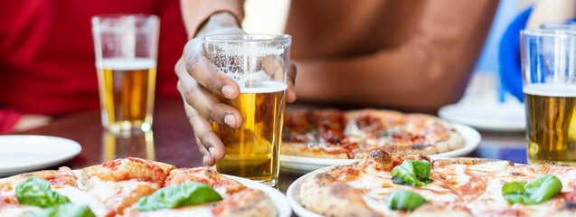 Horizontal banner or header with close-up of african guy's hand taking glass of beer at pizza...