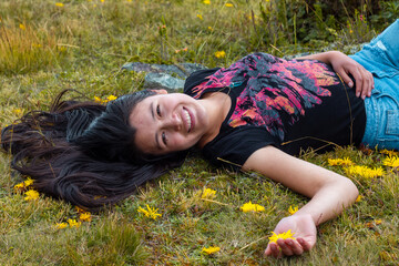 Atractiva mujer tirada en la hierba después de una caminata y sonriendo a la cámara