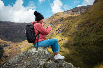 Naklejka premium Excursionista atractivo sentado y sosteniendo un teléfono junto a un lago tranquilo en las hermosas montañas