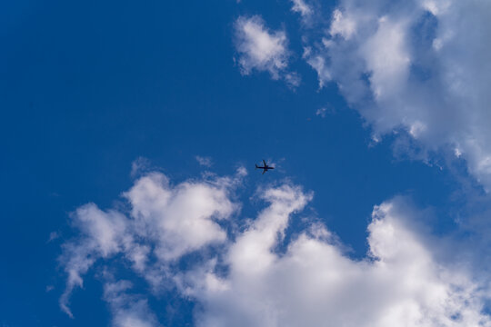 a plane flying against the background of a blue sky with beautiful white clouds, a photo from below, the plane is far away in the photo, the sun is shining from behind the clouds