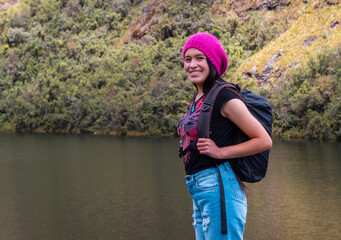 Atractiva excursionista sonriente de pie junto a un tranquilo lago en las hermosas montañas.