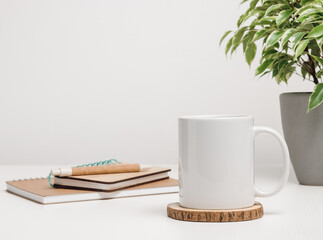 White mockup mug with notepad and houseplant at the background, mug with copy space for logo, text and design
