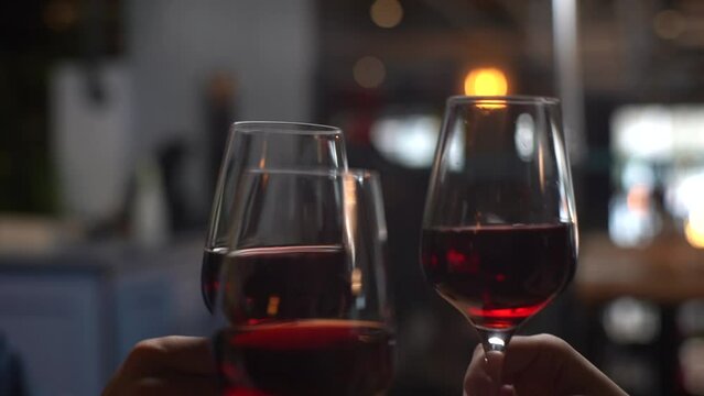 Close-up hands of unrecognizable man and women clinking with wine glasses during festive dinner at table in luxury restaurant on blurred background of bokeh lights. Shooting in slow motion.
