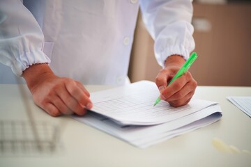 A lab technician in a white coat writes notes on a document, indicating data recording and...