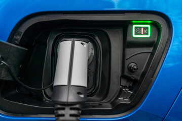 Illuminated unlocking Botton on a blue electric car with the charging connector plugged in