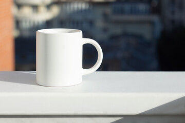 A white mug on the windowsill with a view of the city - 525352231