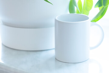 A white mug on the windowsill near the plant. White soft minimalist high key picture. - 525352235