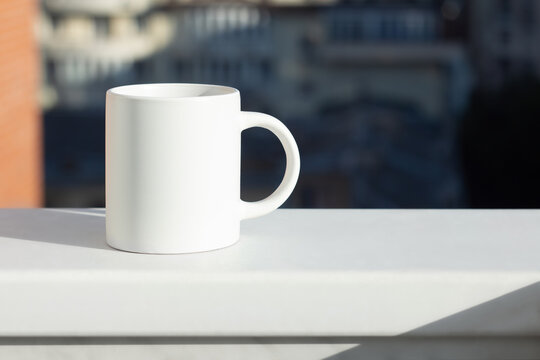 A white mug on the windowsill with a view of the city