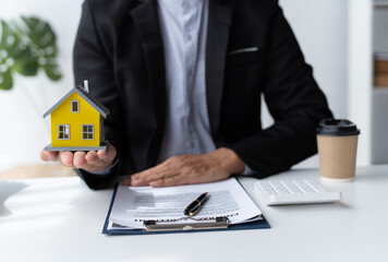 A real estate broker or insurance agent works with home models and home real estate sales contracts within the office, Mortgage loan approval home loan and insurance concept.