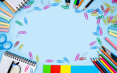 Colorful school stationery lie in the shape of a frame on blue background. Back to school. Flatlay composition. Top view. Copy space.