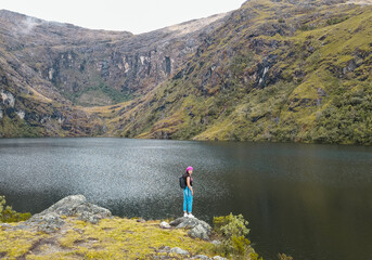 Hermosas montañas y mujer joven de pie con mochila en un lago. Paisaje con chica deportiva en la...