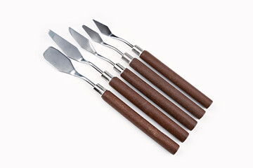 Art palette knives lie on a white art canvas. ainless painting palette knife with wooden handle. Palette knives, isolated on white. set new painting palette knives.