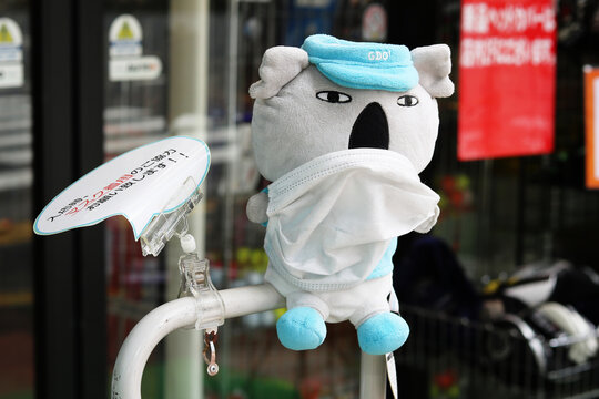 TOKYO, JAPAN - August 12, 2022: Soft toy koala bear wearing a face mark at the front of a golf store. The sign asks customers to wear face masks due to coronavirus. 