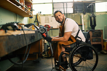 A man in the wheelchair does metalwork in his workshop.