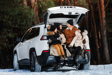 Happy young family is traveling by car in winter forest. People have fun together. Mom, dad and children on winter walk.