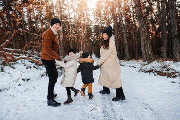 Happy young family walks through the winter forest holding hands. Parents and children on a winter walk.