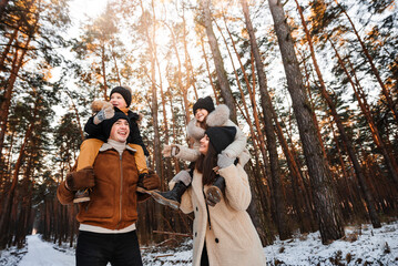 Young happy family on a winter walk. Cheerful children riding on shoulders. Mom and dad carry two small, laughing kids on their shoulders.