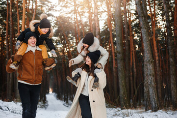 Father and mother with two small children in winter nature, walking in the snow. Happy family spending time together.