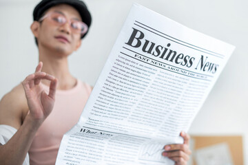 Satisfied LGBTQ guy reading newspaper while sitting in her studio, look happy when read good news...