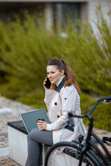 Fototapeta premium woman speaking on smartphone and using laptop outdoors in city