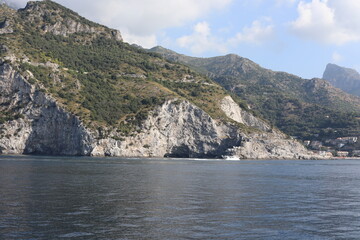 Fototapeta premium Rocky coast of the island. Scenic Amalfi Coast view from the sea. Beautiful seascape with yacht near shore in sea. Modern sailboat on a sunny summer day. Sailing near coastline in Mediterranean Sea.