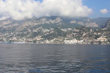 Scenic Amalfi Coast view from the sea. Beautiful seascape with yacht near shore in the sea. Modern sailboat on a sunny summer day. Sailing near coastline in the Mediterranean Sea.