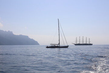 Fototapeta premium Beautiful seascape with yacht near shore in the sea. Modern sailboat on a sunny summer day. Sailing near coastline in the Mediterranean Sea. Scenic Amalfi Coast view.
