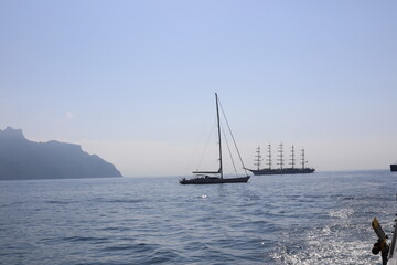 Fototapeta premium Beautiful seascape with yacht near shore in the sea. Modern sailboat on a sunny summer day. Sailing near coastline in the Mediterranean Sea. Scenic Amalfi Coast view.