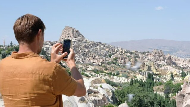 Tourist man in takes a photo on the phone in valley in Cappadocia in Turkey. Guy making video  of beautiful landscape with mobile camera, dreamy travel concept.