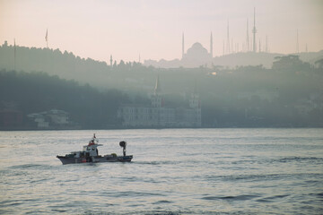 Turkish fisherman sailing in boat in sea. The view of Kuleli Military High School and Camlica Mosque from the Bosphorus.  - Powered by Adobe