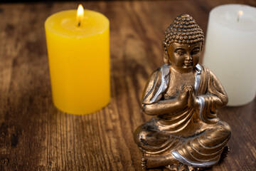 Meditating Buddha with lit candle decoration on a wooden table. yellow candlde