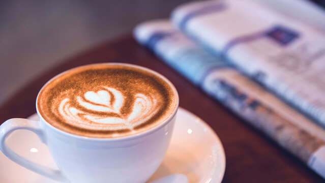 Top view of a Late art coffee cup on blur newspaper background, classic retro warm tone	