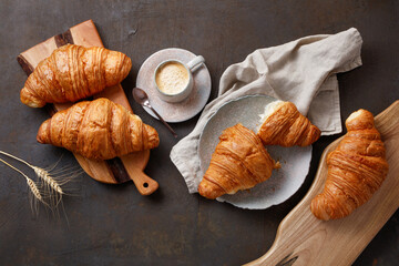 Kitchen boards, plate with tasty croissants and cup of coffee on dark table, closeup. French pastry. Top view