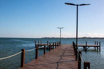 Wooden pier with lampposts at Sao Pedro da Aldeia beach on a sunny day, Cabo Frio, Brazil.