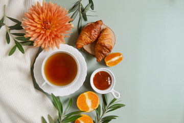 Cup of tea with jam and oranges on the pastel green background. Frame. Stay healthy in flu winter autumn days. Autumn fall tea composition with empty place for text. Calm cozy atmosphere. Village vibe