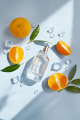 Glass bottle of perfume with oranges, green leaves, ice cubes, water drops on the light blue background with day sunlight. Smell of summer. Fresh orange cooling perfumery.  Direct sun rays. 