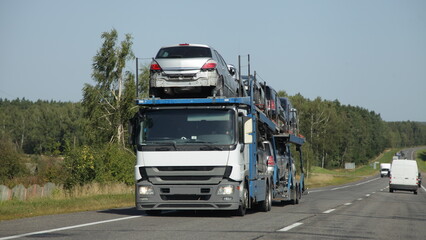 Loaded car carrier truck with old cars transporter semi trailer drive on suburban highway road at summer day, front side view. European used cars export in Russia with sanctions