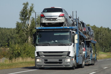 Obraz na płótnie Canvas Loaded two level car carrier truck with car transporter semi trailer drive on suburban highway road at summer day, front side view. Delivery autos logistics, automobile transportation