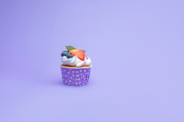 One delicious beautiful cupcake with strawberries and blueberry, white cream and golden sponge cake, in a purple stand with dots on a gently purple