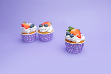 Three delicious beautiful cupcakes with strawberries and blueberry, white cream and golden sponge cake, in a purple stand with dots on a gently purple background, perfect for birthday 