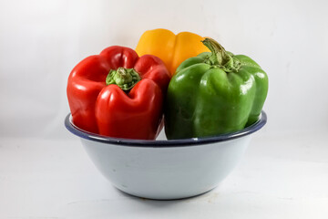 Green, red, yellow bell peppers in white ceramic bowl