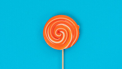 Round orange lollipop on a stick on a blue background - juicy sweet background