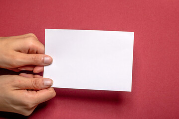 Obraz premium two female hands holding a blank piece of paper with copy space in front of a red background cardboard