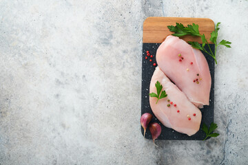 Chicken breast. Two Chicken fillet with spices, olive oil and parsley on black stone cutting board on grey stone table background. Top view with copy space. Food meat cooking background.