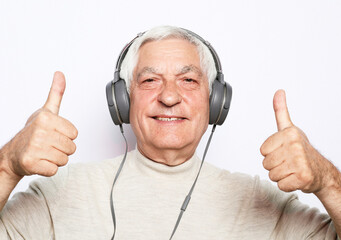 Handsome old man in casual wear and headphones is listening to music using a mobile and smiling, show thumbs up