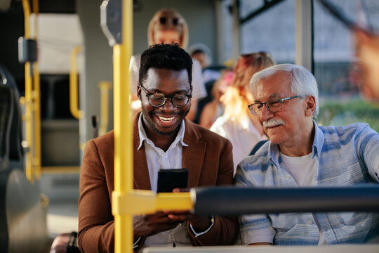 Black man showing senior caucasian man smartphone on public transport